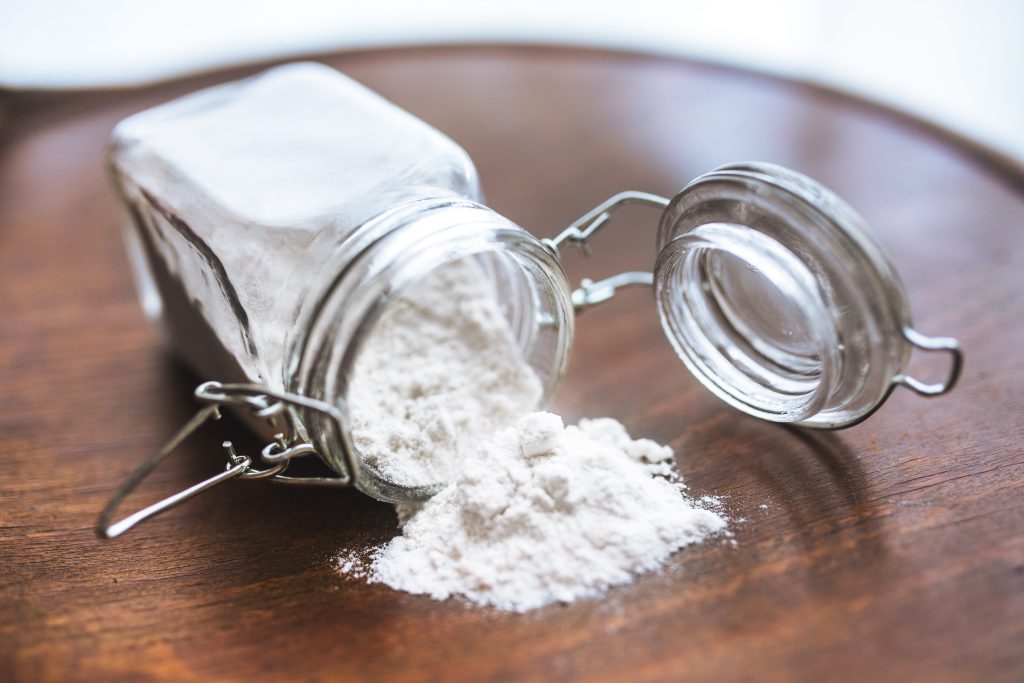 Flour in a jar pouring out on a wooden table